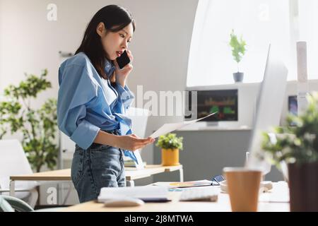 La signora che tiene il rapporto di lettura della carta che parla al telefono all'ufficio Foto Stock