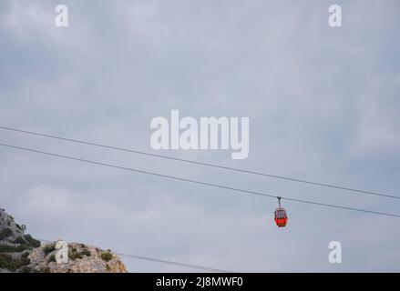 Cabine rosse di funicolare ad Antalya, Turchia sullo sfondo di nuvole di pioggia. Gita in funivia ai punti panoramici delle montagne. Durante il viaggio in funivia i turisti godono di splendide vedute della città e della natura Foto Stock