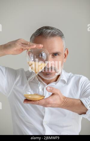 Uomo in camicia bianca con un orologio a sabbia nelle mani Foto Stock