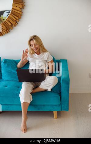 Bella donna caucasica allegra ondeggiando con la mano alla webcam e facendo video chat sul portatile. Foto Stock