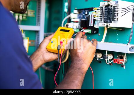 Tecnico elettrico a spalla o riparatore che controlla il collegamento utilizzando il voltmetro sul quadro di distribuzione dell'alimentazione dell'azienda industriale - concetto di Foto Stock