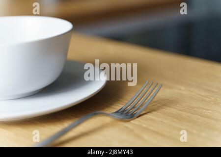 Ciotola bianca in ceramica con cibo e forchetta su un tavolo in legno in cucina in un ristorante o a casa. Messa a fuoco selezionata. Foto di alta qualità Foto Stock