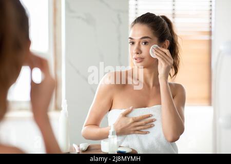 Graziosa donna che usa il tampone di cotone che pulisce la pelle facciale in bagno Foto Stock