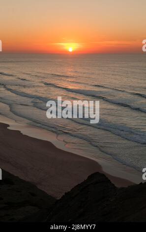 Tramonto invernale che si affaccia sull'Atlantico dall'Algarve occidentale, Portogallo. Surfers nelle onde qui sotto. Novembre. Foto Stock