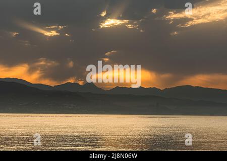 Alba estiva, con skyline di montagna e luce del sole dorata che si infrangono attraverso le nuvole tempestose. Costa del Sol, Malaga, Spagna. Foto Stock