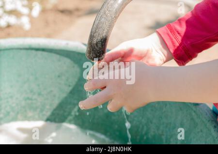 Il bambino si lava le mani, da vicino. Primo piano delle mani del bambino sotto un rubinetto nel cortile Foto Stock