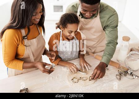 Famiglia nera che usa le forme di cottura che fanno i biscotti in cucina Foto Stock