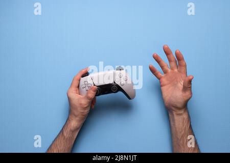 Tenere premuto il nuovo joystick. Il giocatore gioca con il controller gamepad. Uomo di gioco che tiene il joypad simulatore. Persona con tastiera gioiosa in braccio. Non discreto Foto Stock