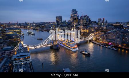 Vista aerea dello skyline di Londra con una nave da crociera con movimento sfocato che passa sotto il Ponte della Torre sollevato Foto Stock