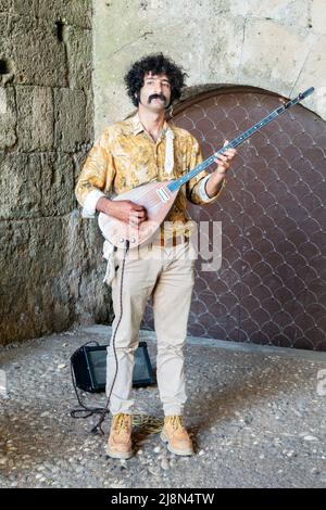 Un busker maschile che suona un bouzouki, uno strumento a corde greco. Il musicista si trova in un'alcova nel centro storico di Rodi, in Grecia Foto Stock