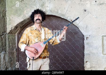 Un busker maschile che suona un bouzouki, uno strumento a corde greco. Il musicista si trova in un'alcova nel centro storico di Rodi, in Grecia Foto Stock