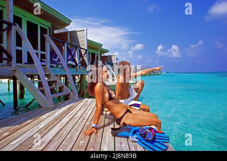 Coppia seduta su una piattaforma presso i bungalow sull'acqua, Kuredu, Atollo Laviyani, Oceano Indiano, Asia Foto Stock