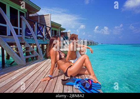 Coppia seduta su una piattaforma presso i bungalow sull'acqua, Kuredu, Atollo Laviyani, Oceano Indiano, Asia Foto Stock