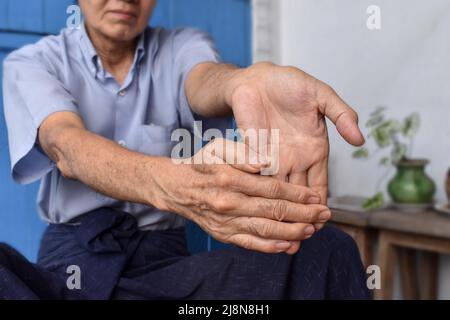 Rafforzamento dell'esercizio per i muscoli del braccio di un paziente maschile anziano asiatico con spasmo muscolare. Foto Stock