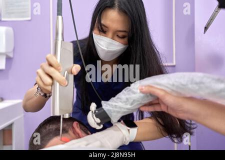 Medico di una clinica che applica il laser ad un paziente per effettuare un trattamento di bellezza della pelle Foto Stock