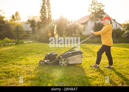 Giovane donna che taglia erba con un rasaerba. Concetto di attività all'aperto per la casa. Foto Stock