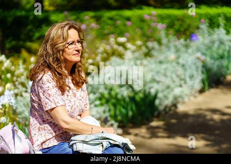 Ritratto di una donna bianca seduta in un parco con più fiori non focalizzati. Foto Stock
