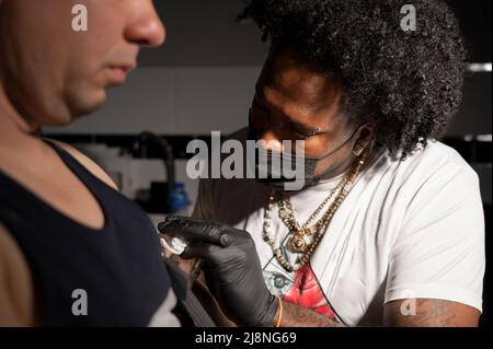 L'artista professionista del tatuaggio afroamericano fa un tatuaggio sul braccio del cliente. Fotografia di alta qualità. Foto Stock