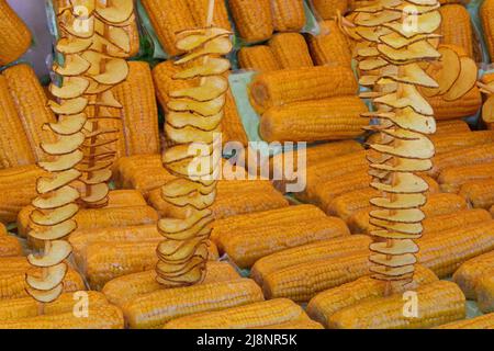 molti cellophane gialli hanno avvolto le pannocchie di mais e molti spiedini di patate fritte con la buccia per la vendita in stalla street food Foto Stock