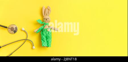 Stetoscopio con attrezzatura medica e giocattolo dal design minimale isolato su sfondo giallo. Salute bambini concetto medico. Simbolo pediatra. Banner dello spazio di copia del layout della vista dall'alto con disposizione piatta Foto Stock