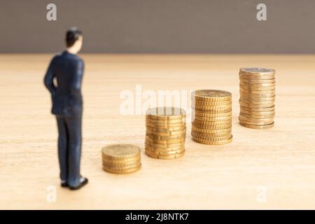 Figurine di businessman che guarda la crescita di una pila di monete. Risparmio di denaro per il concetto di contabilità finanziaria. Spazio di copia Foto Stock