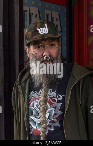 L'uomo pesantemente trafitto con una lunga barba intrecciata grigia, vestita casualy, si trova in una porta Foto Stock