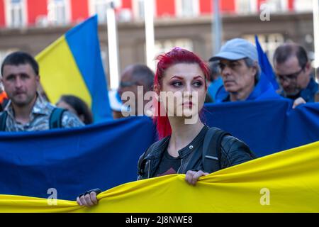 Una donna di testa rossa si erge tra le altre persone che detengono una grande bandiera Ucraina alla marcia Support Ukraine a Sofia, Bulgaria Foto Stock