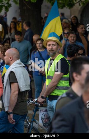 Sofia, Bulgaria - 09 maggio 2022: Un uomo, vestito in un gilet giallo e cappello giallo-blu, si erge in una folla, tenendo la sua bicicletta, con Ukranian f Foto Stock