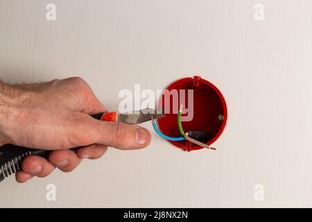 Una mano con un coltello rimuove l'isolamento dei fili in una scatola di giunzione Foto Stock