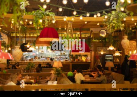 I clienti possono cenare in un bar con lavori in legno, lampade e piante appese in pentole. Foto non messa a fuoco Foto Stock