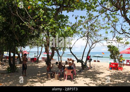 Kuta Beach scena a Bali, Indonesia nel marzo 2022 durante la pandemia con pochi turisti, venditori di bevande, ombrelloni e una spiaggia tranquilla. Foto Stock