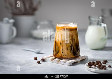 Caffè ghiacciato in un bicchiere trasparente con ghiaccio e latte su sfondo grigio. Foto Stock