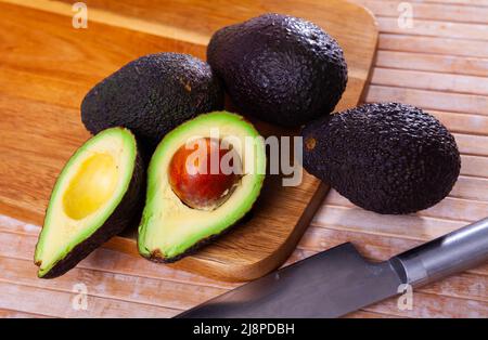 Avocado fresco intero e dimezzato su superficie di legno Foto Stock