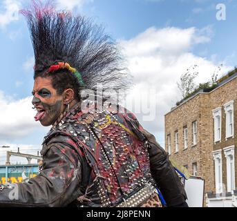 Un rocker punk con una fantastica acconciatura mohawk, lingua divisa, tatuaggi facciali e piercing colpisce una posa arrabbiata per strada. Foto Stock