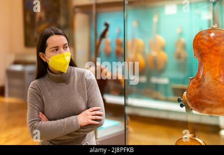 Brunetta in maschera protettiva che visita la mostra di strumenti musicali medievali Foto Stock