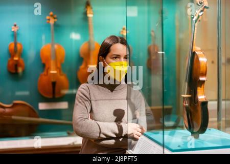 Donna in maschera che guarda collezioni di antichi strumenti musicali in museo Foto Stock