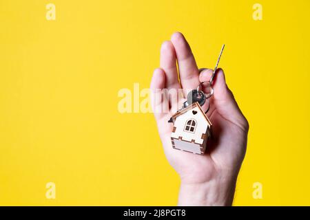 Acquisto di una casa. L'acquirente riceve la chiave per la proprietà. Appartamento ipotecario. Chiavi e una piccola casa in legno in mano. Consegna delle chiavi all'Ora Foto Stock