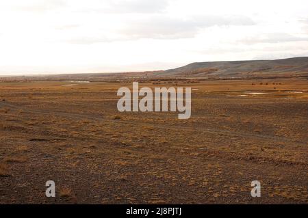 Steppa desertica piatta e sconfinata ai piedi di una catena montuosa all'inizio dell'autunno. Chui steppe, Altai, Siberia, Russia. Foto Stock