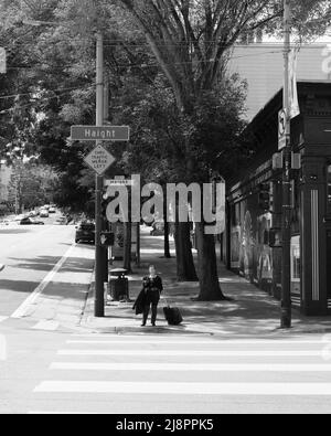 Giovane donna in attesa di attraversare la strada all'angolo di Masonic Avenue e Haight Street; Haight-Ashbury District a San Francisco, California, valigia. Foto Stock