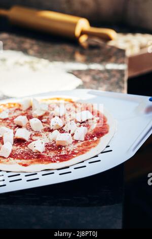 Pizza su una spatola prima di cuocere in forno. Il processo di preparazione della pizza fatta in casa. Il concetto di fast food fatto in casa. Foto verticale. Foto Stock