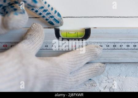 Le mani dell'operatore controllano l'uniformità della parete con un attrezzo speciale per misurare il livello. Il palco di fronte al muro della cucina con piastrelle in ceramica bianca Foto Stock