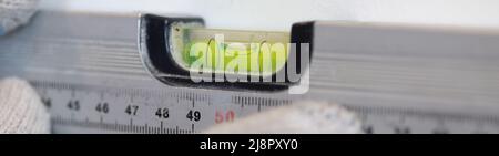 Le mani dell'operatore controllano l'uniformità della parete con un attrezzo speciale per misurare il livello. Il palco di fronte al muro della cucina con piastrelle in ceramica bianca Foto Stock