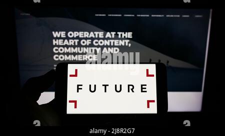 Persona che tiene il cellulare con il logo della società di media britannica Future plc sullo schermo di fronte al sito web aziendale. Mettere a fuoco sul display del telefono. Foto Stock