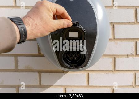 Stazione di ricarica privata per veicoli elettrici montata sulla parete in mattoni accanto al parcheggio Foto Stock