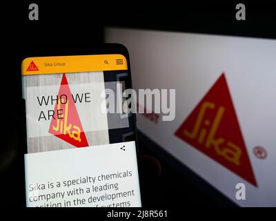 Persona che tiene il cellulare con il sito web della società svizzera di prodotti chimici speciali Sika AG sullo schermo di fronte al logo. Concentrarsi sul centro del display del telefono. Foto Stock