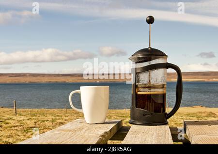 French press con caffè, pronto per essere versato in una tazza bianca su un tavolo di legno in un ampio paesaggio soleggiato e aperto Foto Stock