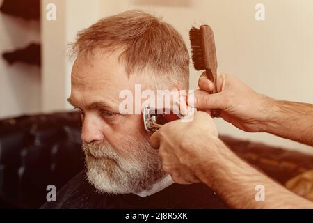 Un uomo anziano che intruda i capelli di un maestro in un barbiere. Un vecchio uomo ottiene un taglio di capelli elegante Foto Stock