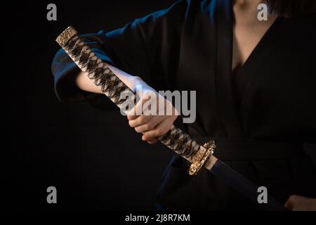 Primo piano sul poggio di una spada giapponese in mano di una donna in un kimono nero. Foto Stock