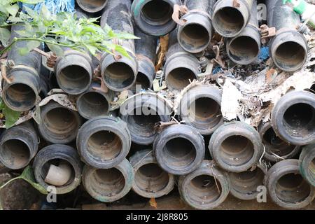 I tubi sono impilati in un luogo che sembra vecchio e sporco. Tubi in PVC utilizzati per scopi di irrigazione abbandonati Foto Stock