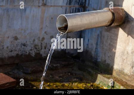 L'acqua pura della sorgente fluisce da un tubo metallico. Foto Stock